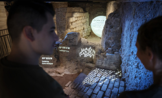 Twee mensen op voorgrond met de gelaagde archeologische vondsten in het museum.