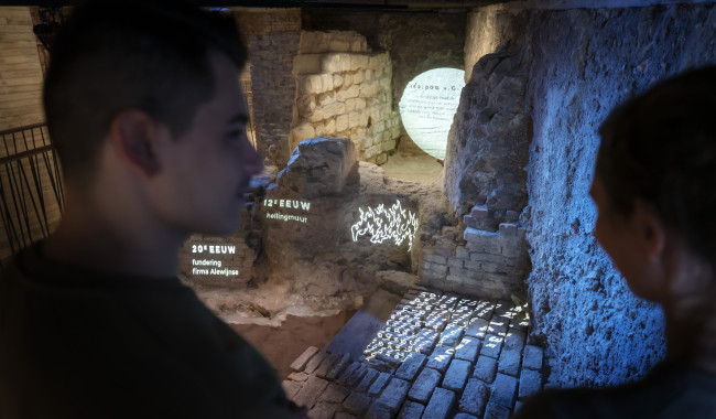 Twee mensen op voorgrond met de gelaagde archeologische vondsten in het museum.