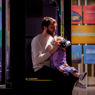 Vader en dochter proberen VR in de tentoonstelling De Grote Reis van Klein Plastic.